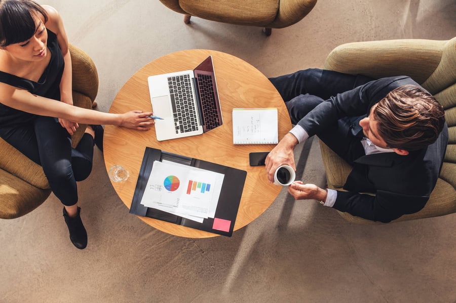 Two people ops professionals at a table with a laptop and printout of HR metrics discuss how 360 degree feedback impacts employee turnover