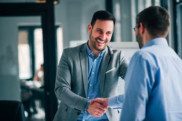 Smiling man in an office receiving a handshake from a colleague to congratulate him on his recent promotion
