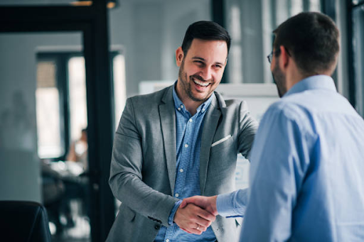 Smiling man in an office receiving a handshake from a colleague to congratulate him on his recent promotion